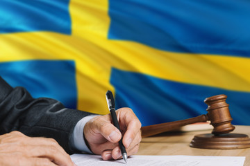 Judge writing on paper in courtroom with Sweden flag background. Wooden gavel of equality theme and...