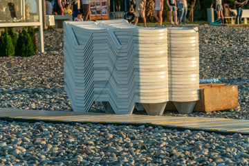 Sunbeds collected in a pile after sunset on the sea with a pebble beach; Batumi