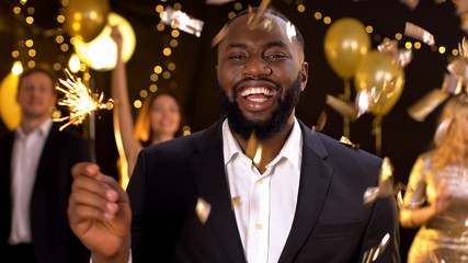 Joyful black male holding bengal light in hand smiling camera, festive event