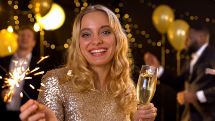 Happy young lady with glass of champagne holding sparkler, new year celebration