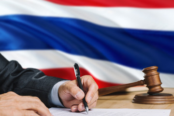 Judge writing on paper in courtroom with Thailand flag background. Wooden gavel of equality theme and legal concept.