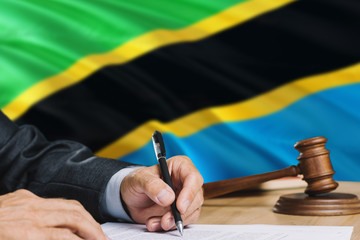 Judge writing on paper in courtroom with Tanzania flag background. Wooden gavel of equality theme and legal concept.