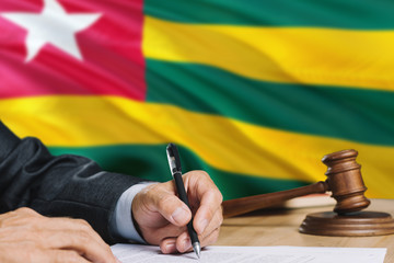 Judge writing on paper in courtroom with Togo flag background. Wooden gavel of equality theme and legal concept.
