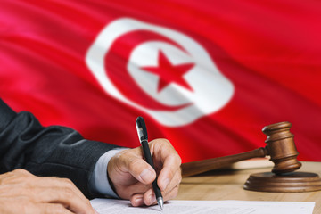 Judge writing on paper in courtroom with Tunisia flag background. Wooden gavel of equality theme and legal concept.