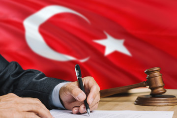 Judge writing on paper in courtroom with Turkey flag background. Wooden gavel of equality theme and legal concept.