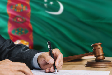 Judge writing on paper in courtroom with Turkmenistan flag background. Wooden gavel of equality theme and legal concept.