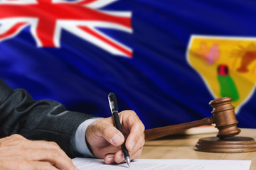 Judge writing on paper in courtroom with Turks And Caicos Islands flag background. Wooden gavel of equality theme and legal concept.