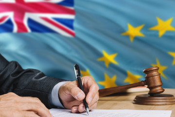 Judge writing on paper in courtroom with Tuvalu flag background. Wooden gavel of equality theme and legal concept.