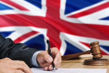 Judge writing on paper in courtroom with United Kingdom flag background. Wooden gavel of equality theme and legal concept.