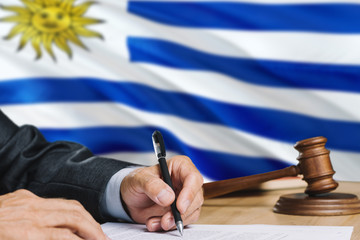 Judge writing on paper in courtroom with Uruguay flag background. Wooden gavel of equality theme and legal concept.