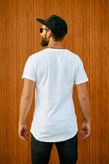 Hipster handsome male model with beard wearing white blank t-shirt and a baseball cap with space for your logo or design in casual urban style