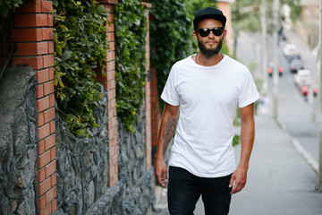 Hipster handsome male model with beard wearing white blank t-shirt and a baseball cap with space...