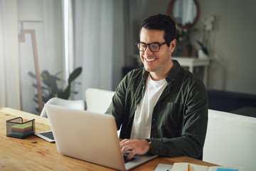 Happy man wearing eyeglasses using laptop at home