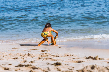 Fototapeta na wymiar little asian girl playing beach tennis on vacation on sandy beach near ocean/sea. travel with kids.