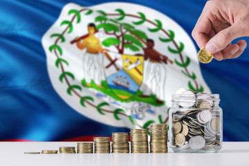 Business man holding coins putting in glass, Belize flag waving in the background. Finance and...