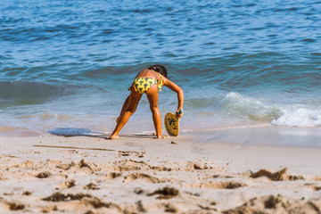 Fototapeta na wymiar little asian girl playing beach tennis on vacation on sandy beach near ocean/sea. travel with kids.