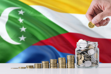 Business man holding coins putting in glass, Comoros flag waving in the background. Finance and...