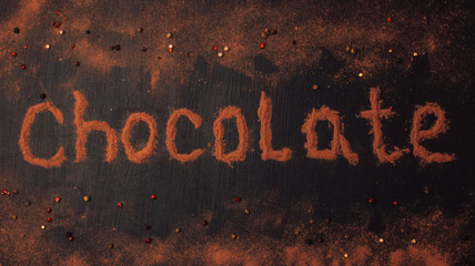 inscription chocolate made of cocoa powder with the addition of pieces of chocolate, chocolate powder, red, black and white pepper on a black graphite background