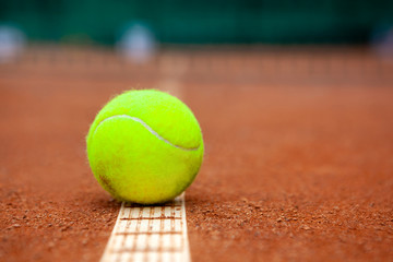A yellow tennis ball lies on the clay court.