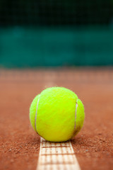 A yellow tennis ball lies on the clay court.