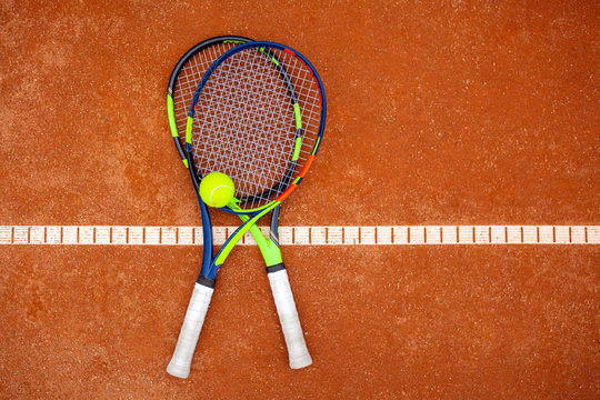 Top view of two tennis rackets and yellow tennis ball lie on the clay court.