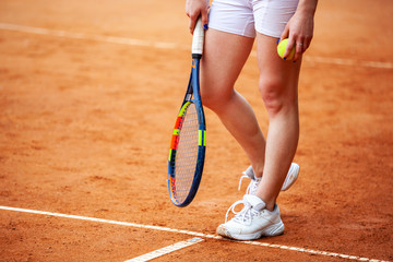 Female tennis player legs in tennis shoes standing on a clay court.