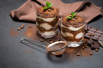 Classic tiramisu dessert in a glass cup, strainer and pieces of chocolate on dark concrete background