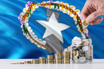 Business man holding coins putting in glass, Northern Mariana Islands flag waving in the background. Finance and business concept. Saving money.