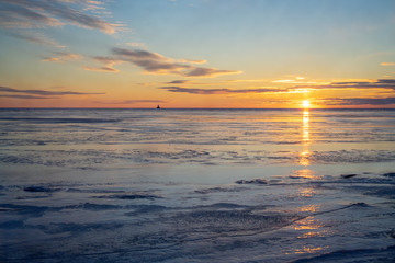 Fototapeta na wymiar The sun setting over a frozen harbor in rural Prince Edward Island, Canada. Lighthouse at the horizon.......