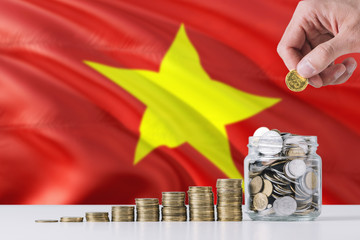 Business man holding coins putting in glass, Vietnam flag waving in the background. Finance and...