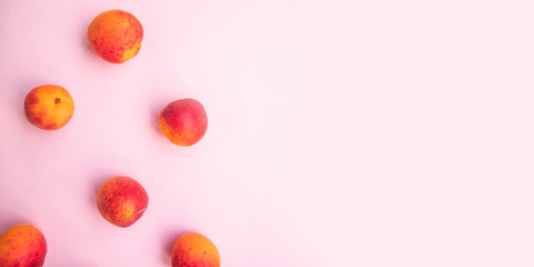 Flat composition of ripe tasty peaches with red side on a pink background.