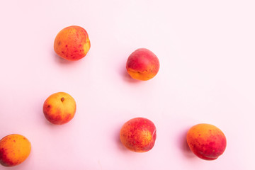 Flat composition of ripe tasty peaches with red side on a pink background.