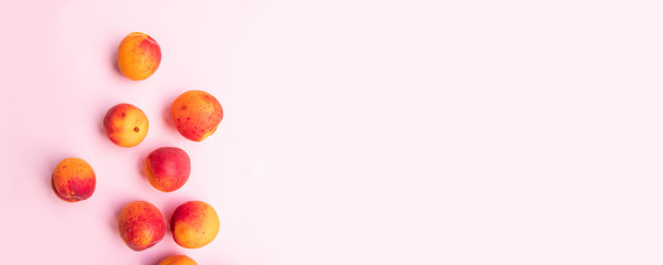 Flat composition of ripe tasty peaches with red side on a pink background.