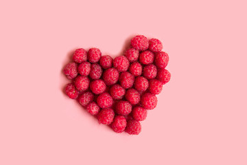 Red raspberries in a heart shape on pink background
