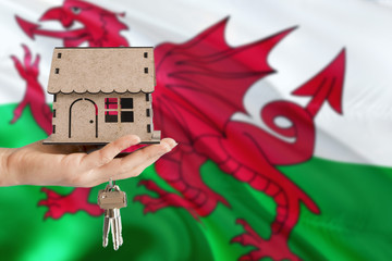 Woman hand holding wooden house and keys with hand. Wales flag with concept of rent, purchase,...