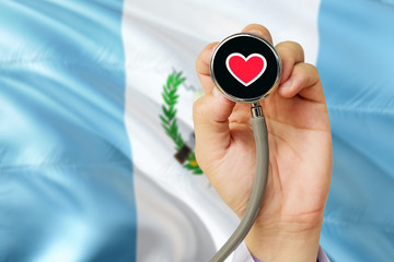 Doctor holding stethoscope with red love heart. National Guatemala flag background. Healthcare system concept, medical theme.