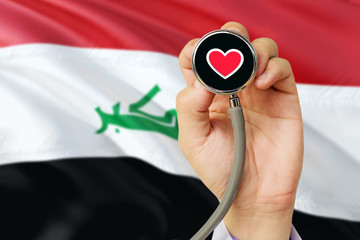 Doctor holding stethoscope with red love heart. National Iraq flag background. Healthcare system concept, medical theme.