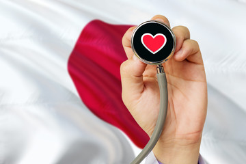 Doctor holding stethoscope with red love heart. National Japan flag background. Healthcare system concept, medical theme.