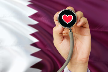 Doctor holding stethoscope with red love heart. National Qatar flag background. Healthcare system concept, medical theme.