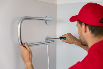 worker installing electric towel dryer on the bathroom wall