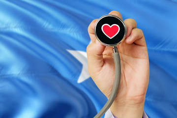 Fototapeta premium Doctor holding stethoscope with red love heart. National Somalia flag background. Healthcare system concept, medical theme.