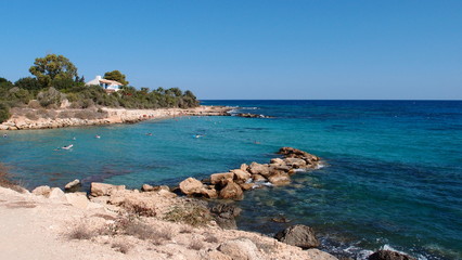 A small rocky spit forms a small bay with a warm transparent turquoise sea and stones at the bottom