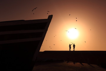 Silhouettes of two people feeding birds at sunset. - 285455690