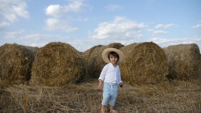 boy in a white shirt and a straw hat is barefoot on a sloping field