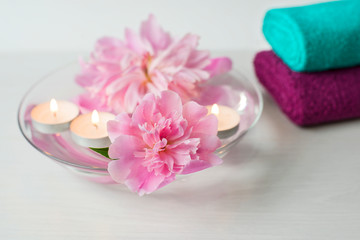 Composition of spa treatment. Pink peonies and candles in the bowl.