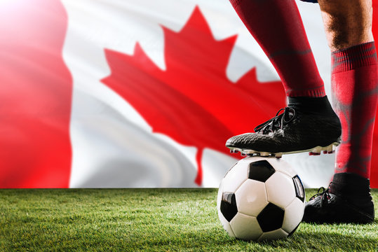 Close up legs of Canada football team player in red socks, shoes on soccer ball at the free kick or penalty spot playing on grass.