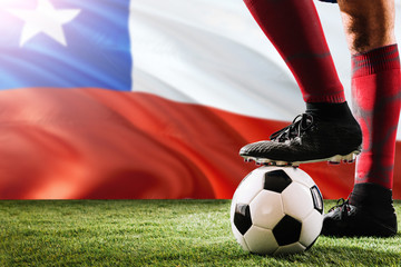 Close up legs of Chile football team player in red socks, shoes on soccer ball at the free kick or penalty spot playing on grass.
