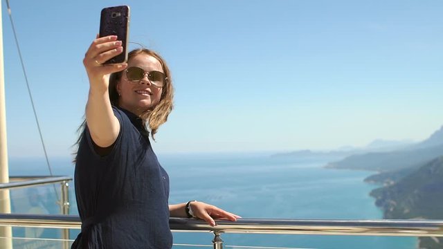 Girl traveler takes selfie with amazing view of sea, mountains, coast. Travel, summer vacation, female tourism concept. Young woman making selfie on a beautiful background of aegean sea and mountains.