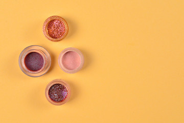 Cosmetics. Makeup. Jars with  crumbly bright shadows, glitter. Pink,peach, golden colors on beige background. Closeup. Space for text or design.