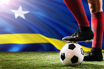 Close up legs of Curacao football team player in red socks, shoes on soccer ball at the free kick or penalty spot playing on grass.